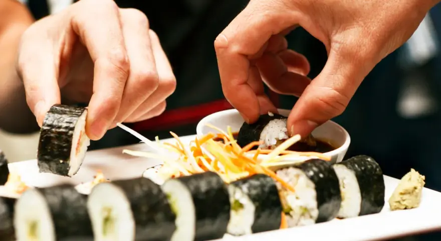 Ręce zanurzają sushi w sosie sojowym. Czy sushi można jeść na drugi dzień? To zależy od świeżości składników i sposobu przechowywania.