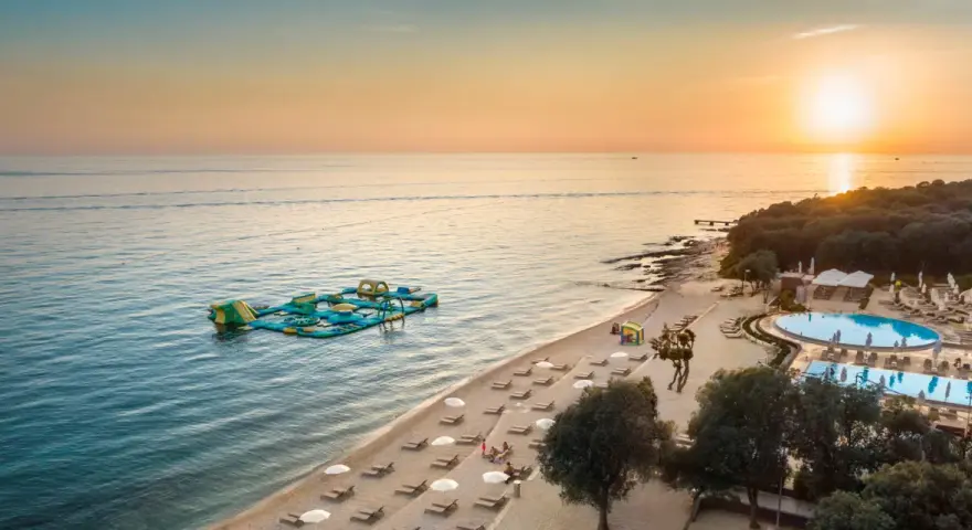 Zachód słońca nad morzem przy plaży z dmuchanym placem zabaw i basenem. Idealne miejsce na wakacje w camping Vrila.
