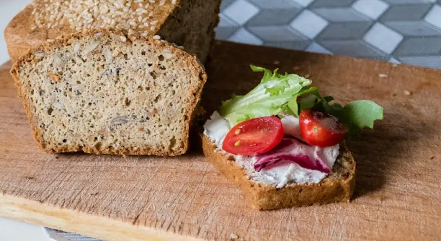 Keto chleb majonezowy przepis: kromka z serkiem, pomidorkami i sałatą obok bochenka z ziarnami.