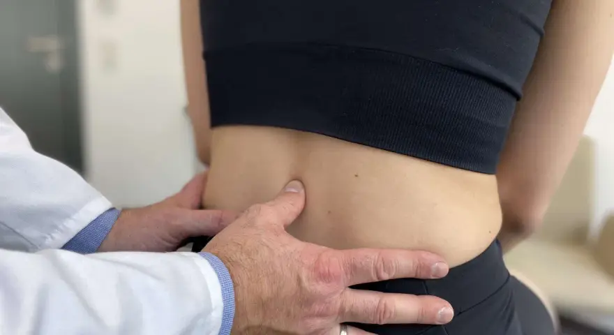 Lekarz bada odcinek lędźwiowy kręgosłupa pacjentki, oceniając objawy spondylozy lędźwiowej.