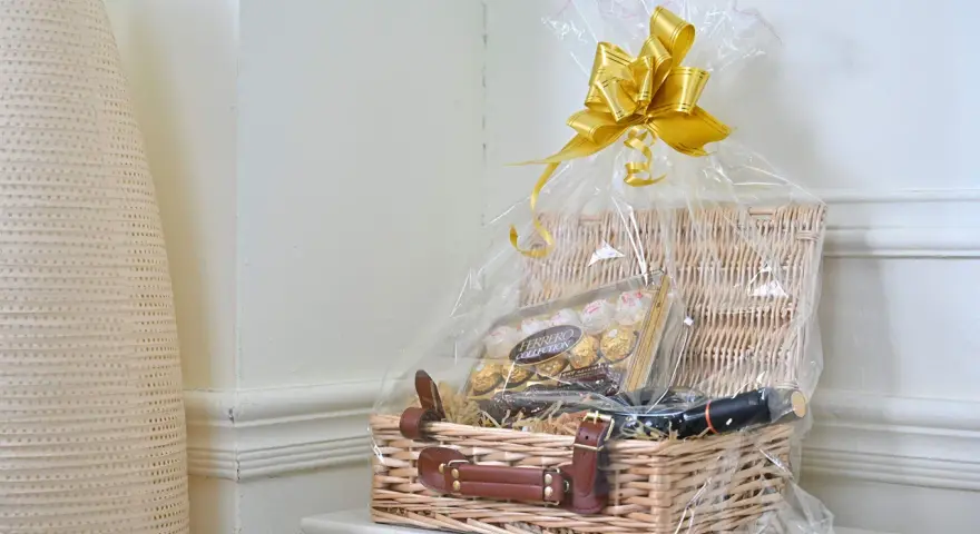 En vacker presentkorg med Ferrero Rocher-choklad och en flaska vin, inslagen i cellofan med en gyllene rosett.