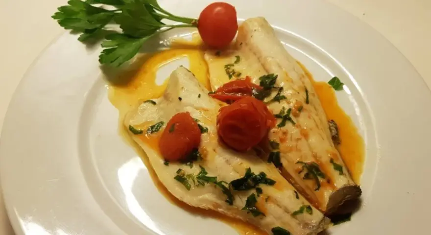 Filetti di branzino in padella con pomodorini e prezzemolo, un piatto leggero e saporito.
