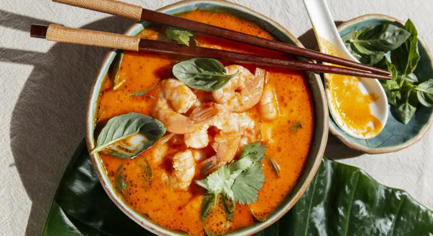 Aksamitna zupa tom yum z krewetkami, ozdobiona świeżą bazylią i kolendrą, gotowa do spożycia pałeczkami.