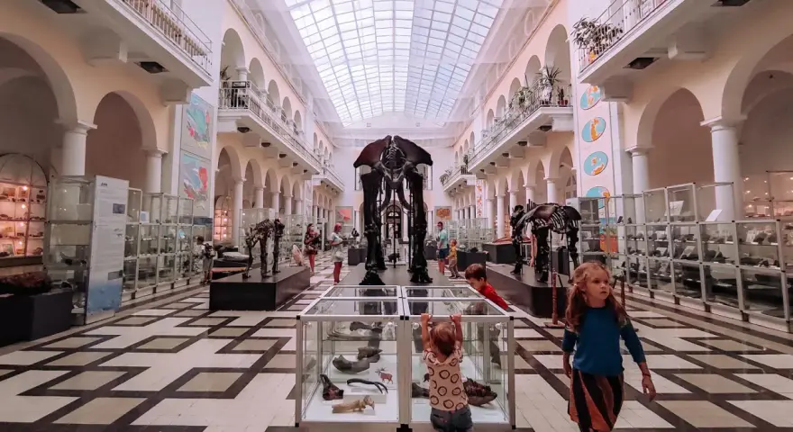 Dzieci zwiedzają muzeum dla dzieci, podziwiając szkielety prehistorycznych zwierząt i wystawy w gablotach.