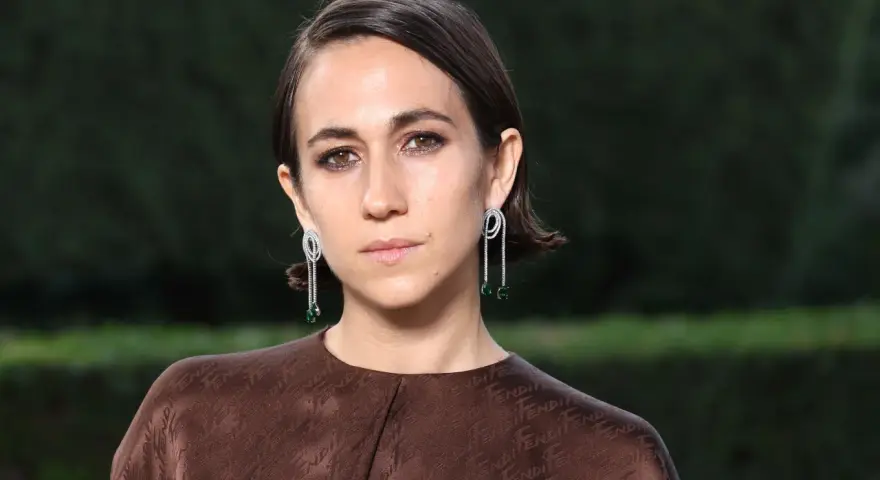 Delfina Delettrez Fendi indossa orecchini pendenti con diamanti e smeraldi, abbinati a un abito marrone con logo Fendi.
