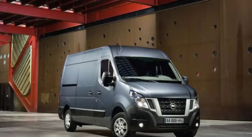 Szary Nissan NV400 stoi przed brązową, perforowaną ścianą w industrialnym wnętrzu.