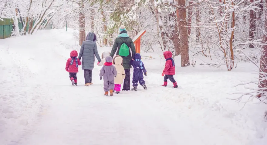 Kindergarten-Pflicht: Eine Gruppe Kinder und Erzieherinnen stapfen durch tiefen Schnee im Wald.