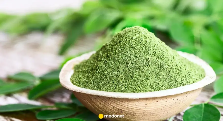 Zielony proszek z liści moringa w miseczce, otoczony świeżymi liśćmi. Odkryj niezwykłe liście moringa właściwości.