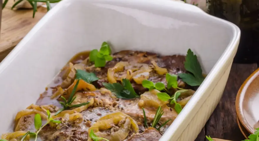 Schab pieczony w piekarniku w naczyniu, duszony z cebulą i ziołami. Aromatyczne danie gotowe do podania.