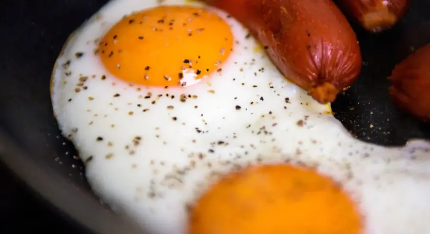 Due uova occhio di bue con pepe nero e salsicce in padella.