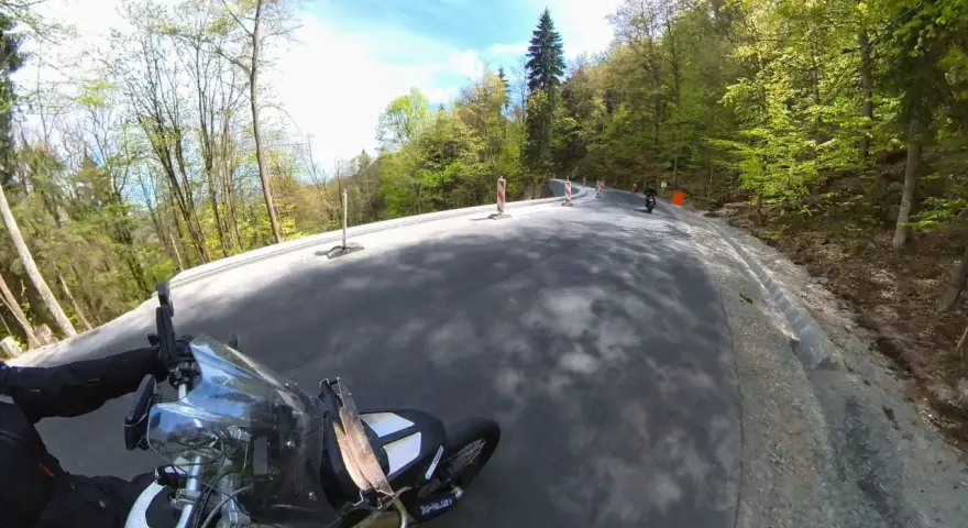 Motocyklista pokonuje krętą drogę stu zakrętów, otoczoną zielonym lasem.