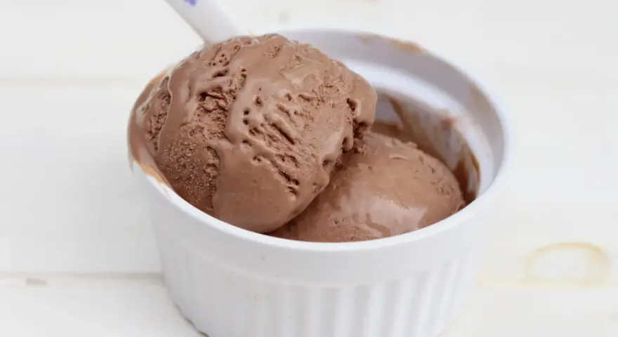 Dos bolas de cremoso helado de chocolate derritiéndose en un cuenco blanco.