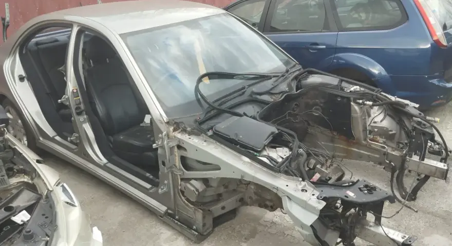 Złomowanie auta: srebrny sedan bez maski i zdemontowanymi częściami, obok niebieski kombi.