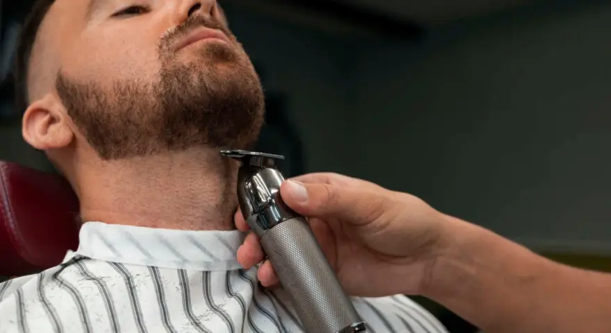 Barbero perfilando la barba ancla de un cliente con una recortadora.