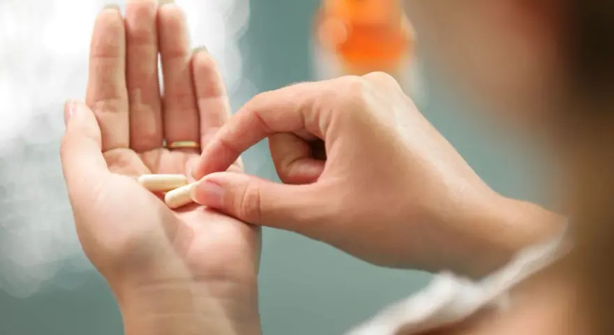 Dłoń trzyma kapsułki, które mogą być lekami do hormonalnej terapii zastępczej.