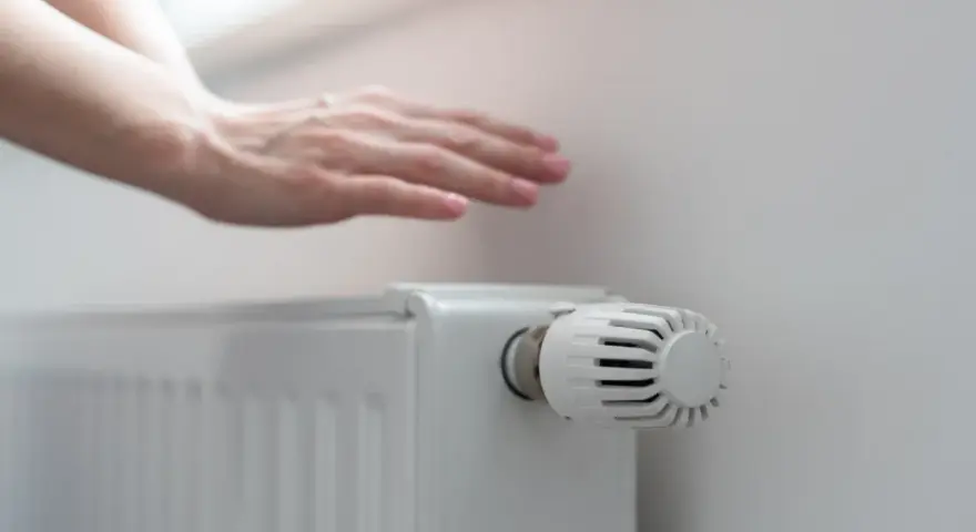 Dłoń nad grzejnikiem, sprawdzająca ciepło. Rozpoczyna się sezon grzewczy, czas na komfortowe ogrzewanie.