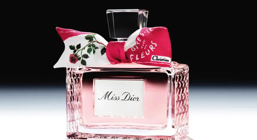 Eleganckie perfumy Miss Dior w różowym flakonie, ozdobione kokardką z motywem róż i napisem "Dites-le avec des fleurs".