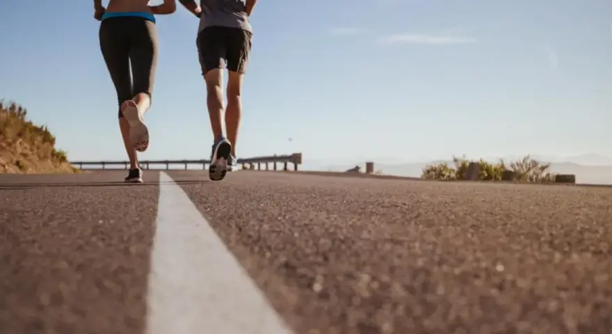 Coppia corre su strada asfaltata, godendosi la libertà e la velocità media corsa sotto un cielo azzurro.