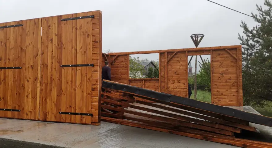 Drewniana wiata w budowie, z widocznymi elementami konstrukcji i bramą.