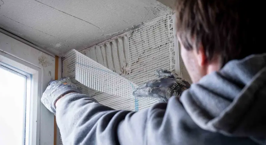 Hand mit Handschuh legt Armierungsgewebe an, um die Fensterlaibung zu verputzen.