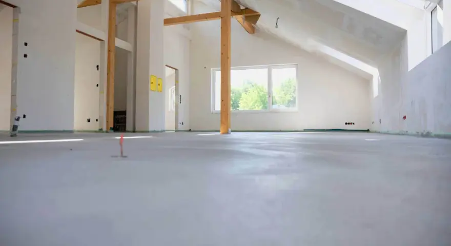 Nowe wnętrze z wylewką samopoziomującą. Widać drewniane belki stropowe i okno z widokiem na zieleń.