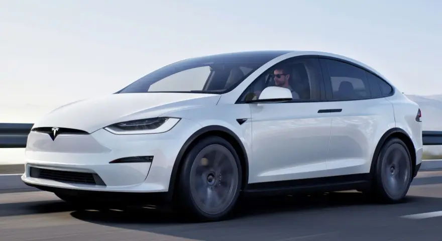 Biały Tesla X w ruchu, kierowca w okularach. Zastanawiasz się nad jego ceną?