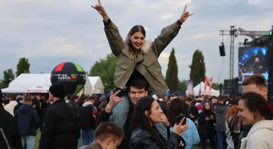 Dziewczyna na ramionach chłopaka cieszy się na Juwenaliach Politechniki Lubelskiej. W tle scena i tłum bawiących się studentów.