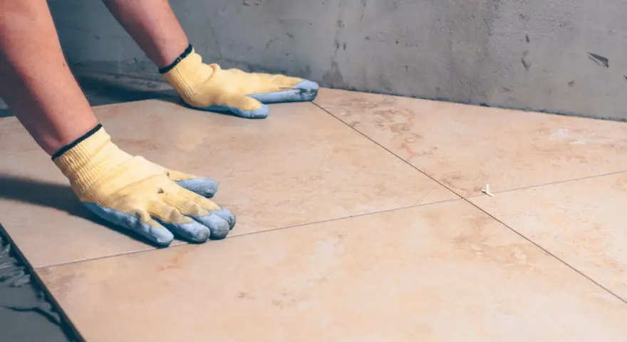 Pose de carrelage : mains gantées ajustant une nouvelle dalle sur la sous couche carrelage.