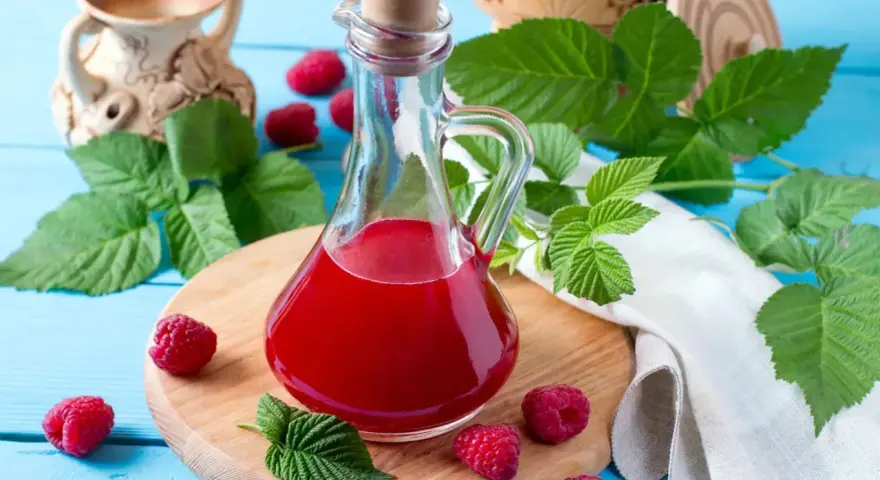 Malinowy ocet balsamiczny do sałatek, deserów, marynat. W butelce z korkiem, otoczony świeżymi malinami i liśćmi.