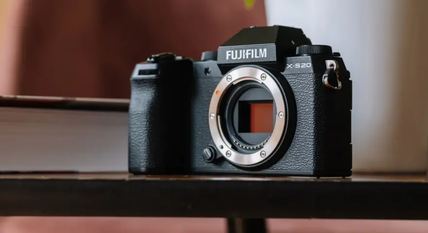 Czarny aparat Fujifilm X-S20 z obiektywem bez obiektywu, leżący na drewnianym stole obok książki.