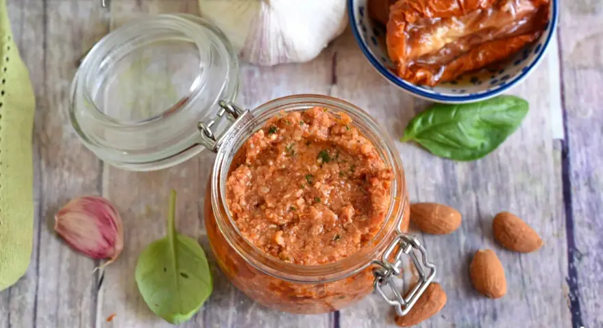 Un vasetto di pesto di pomodori secchi, con mandorle, aglio e basilico, pronto per insaporire i tuoi piatti.