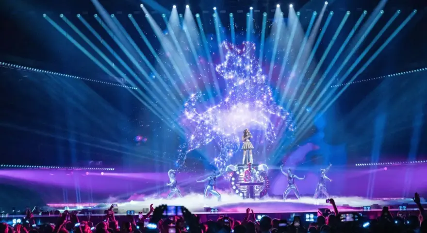 Wokalistka na scenie Eurowizji, otoczona tancerzami i efektami świetlnymi. Widownia filmuje występ, zastanawiając się, ile krajów w finale Eurowizji.