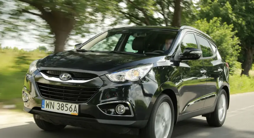 Czarny Hyundai ix35 jedzie drogą wśród zieleni.