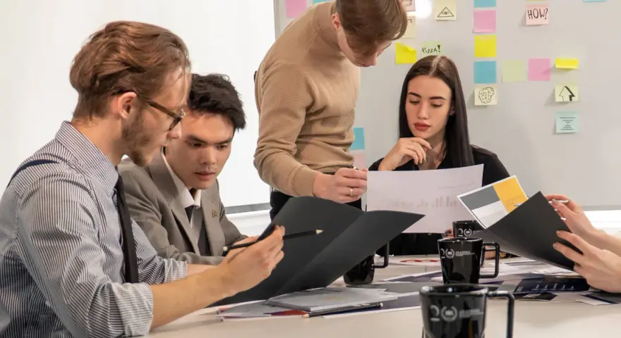 Studenci analizują wykresy, przygotowując się do zajęć z handlu międzynarodowego. Na tablicy notatki i pomysły.