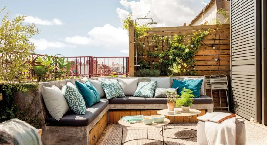 Cómodo rincón de terraza con sofás de obra, cojines turquesas y plantas. Ideas para jardineras exteriores que inspiran relax.