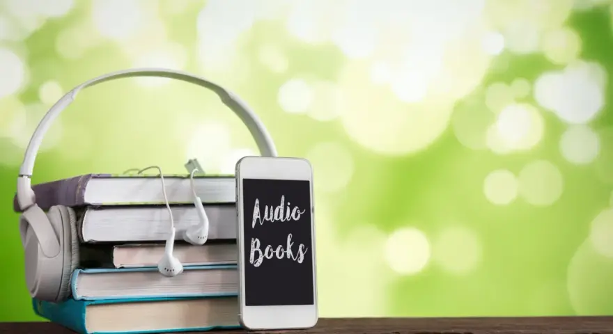 Słuchawki, stos książek i telefon z napisem "Audio Books" – idealne połączenie do odkrywania najpiękniejszych słuchowisk dla dzieci.