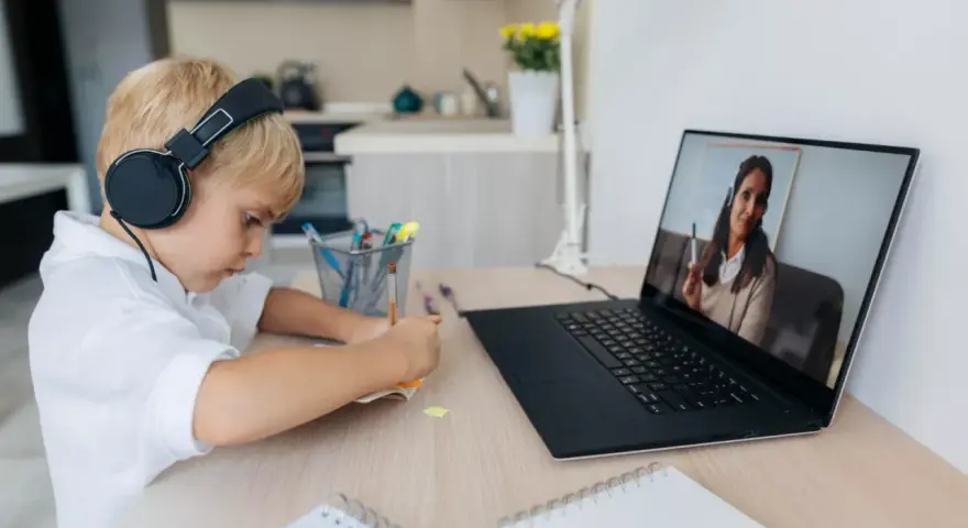 Chłopiec w słuchawkach uczy się zdalnie, patrząc na ekran laptopa z nauczycielem.