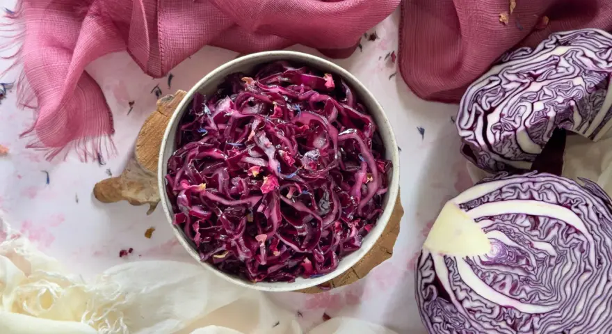 Insalata di cavolo cappuccio rosso, condita con petali di fiori, accanto a un cavolo cappuccio rosso tagliato a metà.