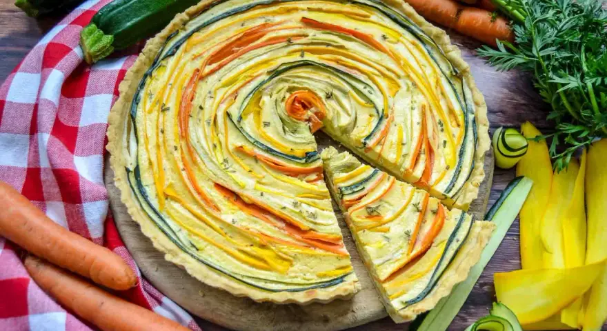 Eine bunte, vegetarische Quiche mit Zucchini und Karotten, kunstvoll im Kreis arrangiert. Frisch und lecker!