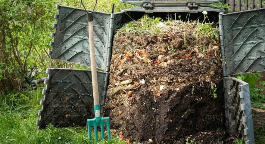 Kompostownik pełen resztek organicznych, obok zielone widły. Proces kompostowania w ogrodzie, numer 200201.