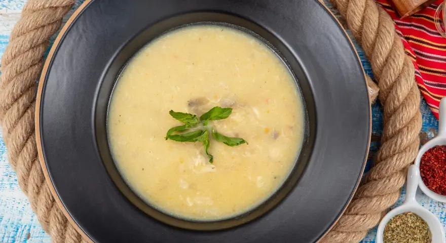 Un plato de sopa de pescado cremoso y caliente, decorado con hojas verdes, sobre un fondo rústico.