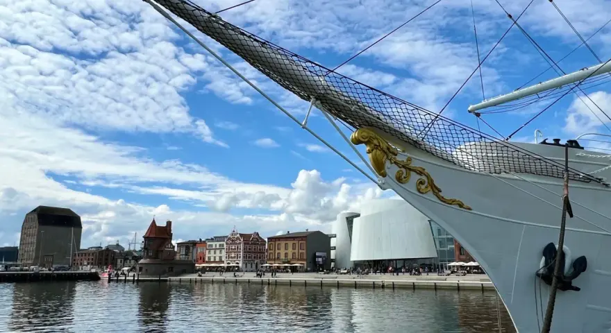 Die Gorch Fock in Stralsund, ein stolzes Segelschiff, liegt vor einer malerischen Kulisse mit historischen Gebäuden und moderner Architektur am Hafen.