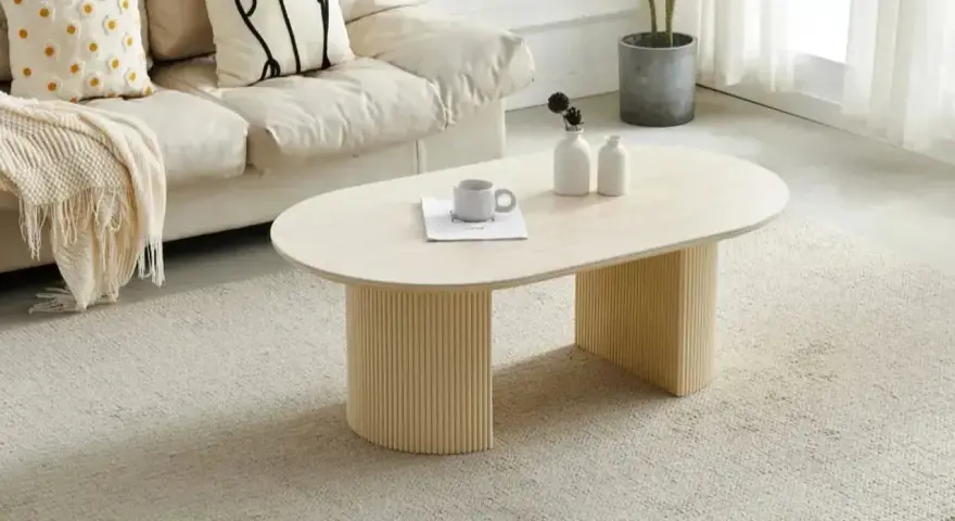 Table basse ovale avec pieds cannelés, sur un tapis doux. Quelle déco avec du travertin, une tasse et des vases sur la table.