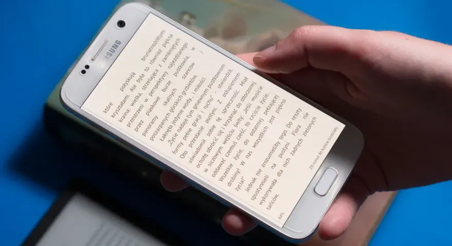 Dłoń trzyma smartfon, na którym wyświetlona jest książka do czytania na telefonie.