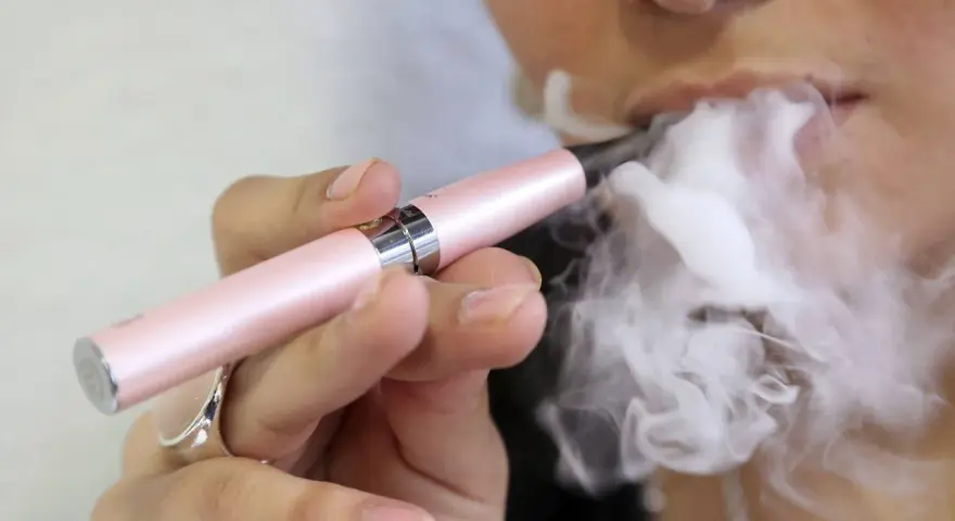 Persona vapea con un dispositivo rosa, liberando vapor. ¿Qué pasa si fumas vaper con nicotina?