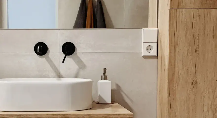 Évier moderne avec robinetterie noire, distributeur de savon et prise électrique. Un détail de la sécurité de la salle de bain.