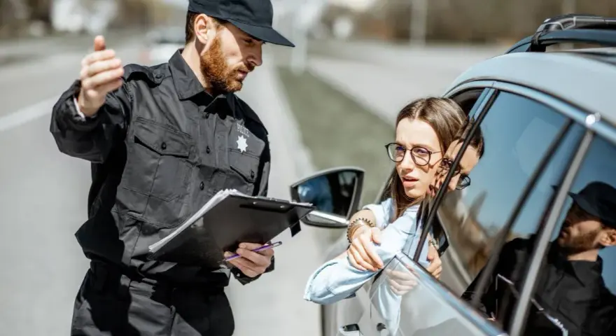 Policjant po 40. zatrzymuje kierowcę do kontroli. Kobieta w okularach wygląda na zaniepokojoną.