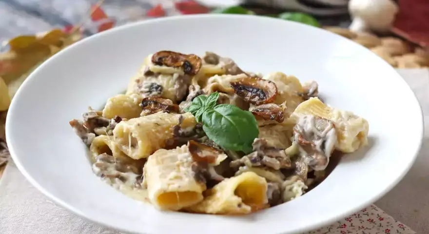 Pyszne spaghetti z grzybami w kremowym sosie, udekorowane listkiem bazylii. Idealne na jesienny obiad.