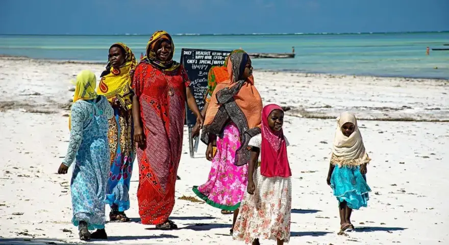 Kobiety w kolorowych strojach spacerują po plaży. Czy Zanzibar to państwo? Tak, to autonomiczny region Tanzanii, znany z pięknych plaż.