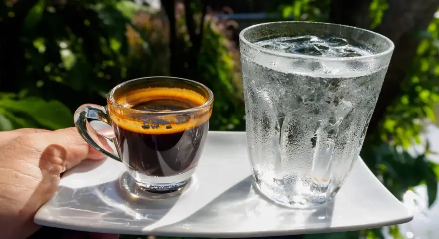 Espresso i szklanka wody z lodem na białym talerzyku. Woda do espresso przed czy po?